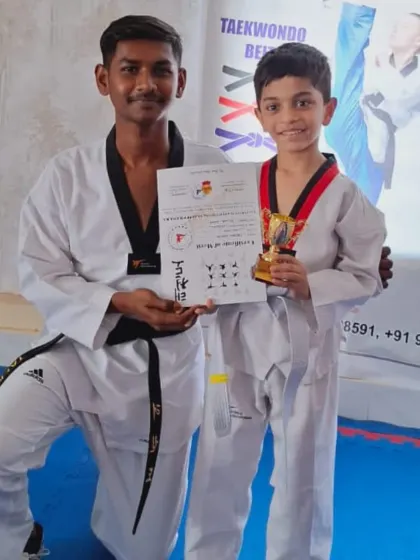 A coach congratulates a young student on his successful belt promotion. He proudly holds his certificate and trophy, marking a new stage in his training.