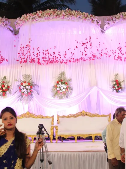 A beautifully decorated stage with white drapes, golden sofas, and a cascade of flowers, ready for the wedding couple.