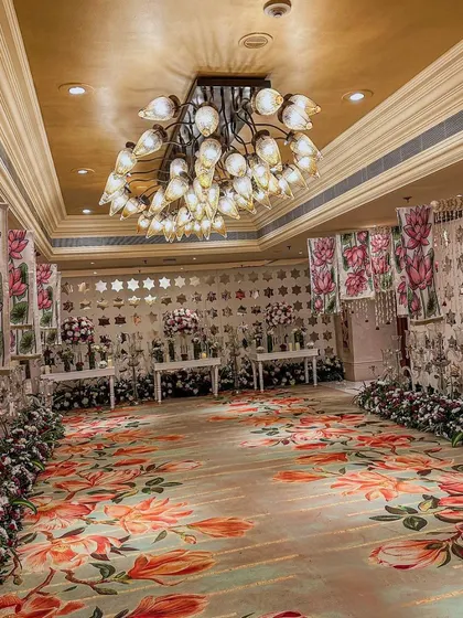 This sangeet hall features a custom floral-printed carpet, lotus-themed wall panels, and a unique chandelier, creating a fully immersive and artistic environment.