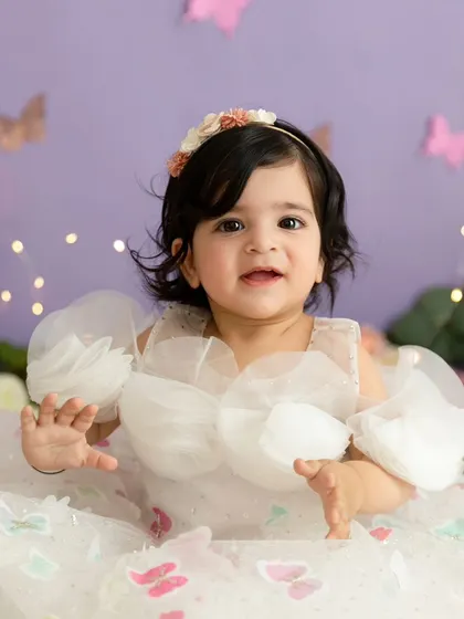A sweet smile from the birthday girl in a beautiful butterfly-adorned dress, part of a whimsical themed session.