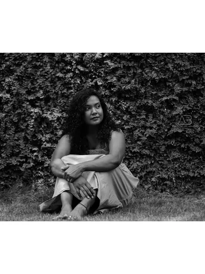 A contemplative black and white portrait. The subject is seated in the grass, and the monochrome tones emphasize the peaceful, natural setting.
