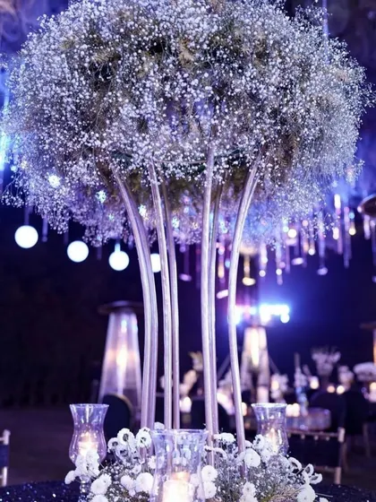 A magnificent centerpiece for a reception table, featuring a large arrangement of baby's breath. The surrounding decor includes hanging crystals and purple uplighting.