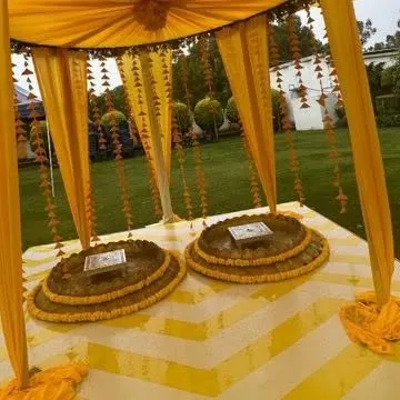 A classic Haldi setup with a canopy of yellow drapes and marigold flower strings. The traditional seating arrangement completes this vibrant and joyful look.