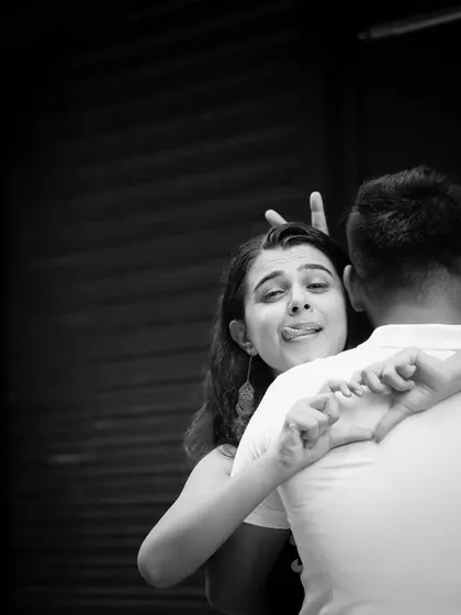 A fun and quirky black and white photo from a pre-wedding shoot. The bride-to-be makes a playful face while hugging her partner from behind, showing their fun-loving personalities.