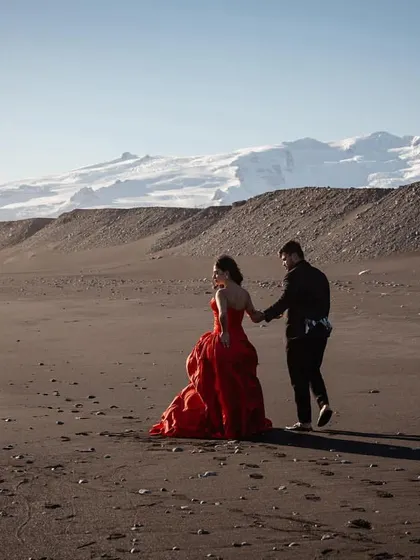 Shree and Abhishek walking on the black sand beaches of Iceland. Her dramatic red gown and his classic black textured suit create a stunning contrast against the landscape.