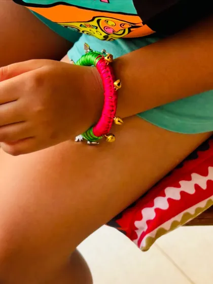 A close-up of the bangle on the wrist, showing how the bright pink and green colors pop. The little bells add a playful, musical element.