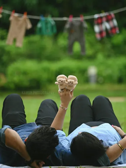 A creative and symbolic maternity shot, with the couple lying on the grass holding up a pair of tiny baby shoes.