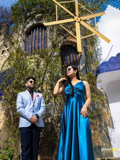 A stylish portrait of a couple posing in front of a rustic building with a windmill, showcasing a unique and picturesque location.