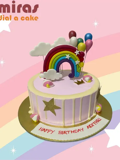 A cheerful rainbow-themed cake with a pink drip. Topped with a colorful rainbow and balloon cluster, this cake is pure happiness and perfect for a bright celebration.