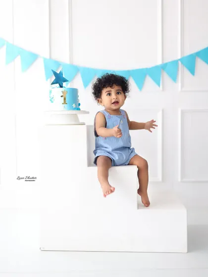 Before the cake! A sweet portrait of the birthday boy in a blue romper, sitting patiently next to his beautiful star-themed first birthday cake.