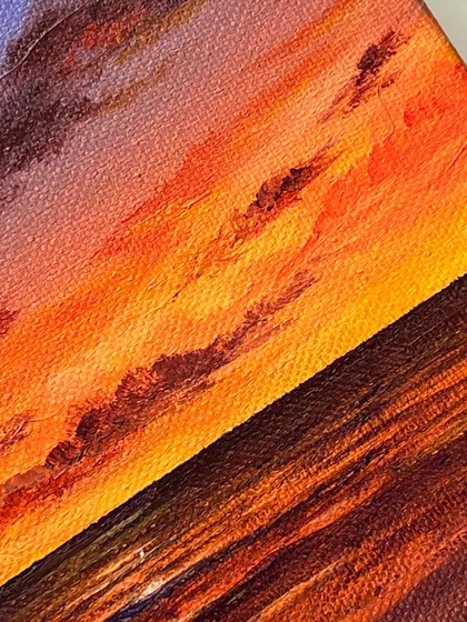 A close up, detailed shot of the textured brushstrokes in a vibrant sunset painting. You can see how the colors are layered to create depth and movement.