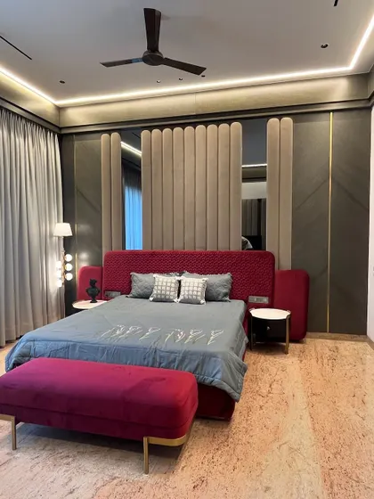 For this master bedroom in Ambala, we used a bold maroon fabric for the custom quilted bed and bench. The tall, upholstered wall panel behind it combines soft textures with mirror and veneer, creating a statement of pure luxury and comfort.
