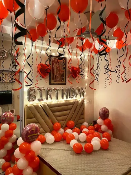 An orange and white themed birthday room setup with foil letters and balloons with ribbons covering the ceiling.