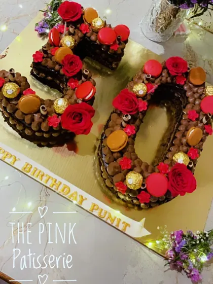 A rich chocolate number cake for a 30th birthday. The "30" is decorated with chocolate piping, Ferrero Rocher chocolates, red macarons, and fresh red roses.