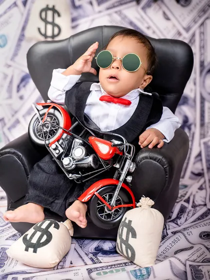 The boss baby takes a break. This little one relaxes in his chair with a toy motorcycle, looking cool and collected in his suit and bow tie.