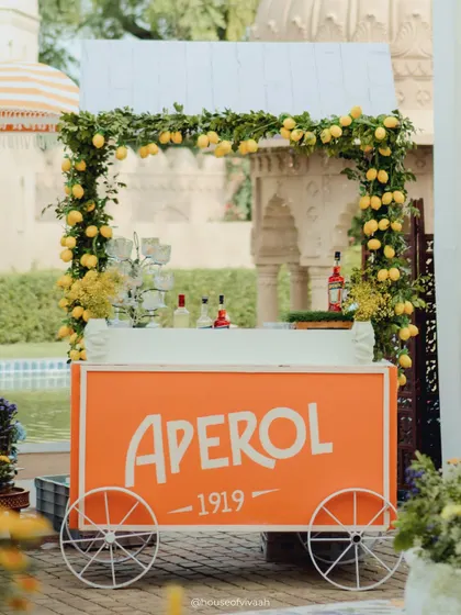A bright orange Aperol cart, adorned with a garland of fresh lemons, perfectly capturing the Italian summer vibe of the Positano-themed event.