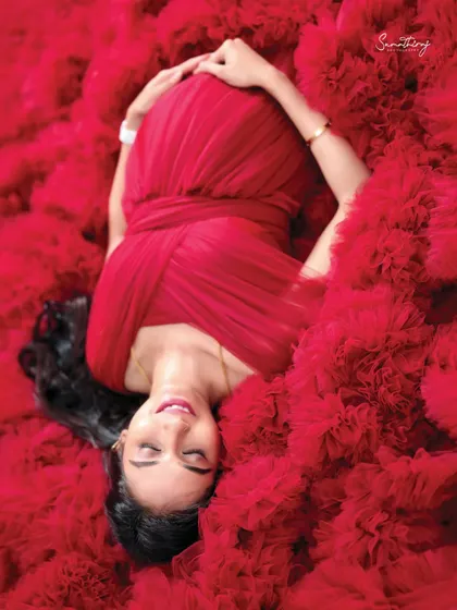 A serene top-down shot of a mother-to-be in a red ruffled gown. Her peaceful expression and the sea of red fabric create a powerful and artistic image.