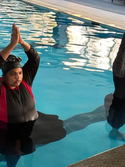 Two participants in a seated prayer pose with arms overhead. This gentle backbend feels wonderful with the support and freedom the water provides.