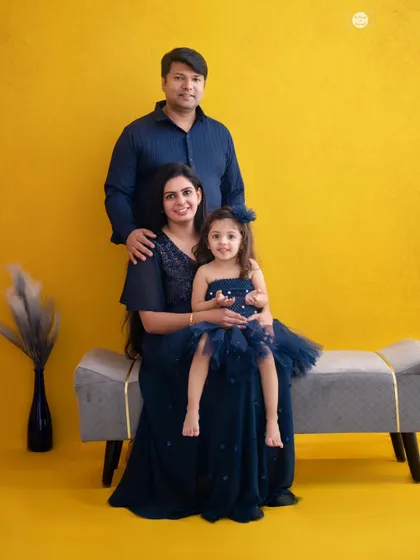A formal family portrait using a bold, solid-colored backdrop. The coordinated navy blue outfits create a cohesive and polished look, making this a timeless keepsake.