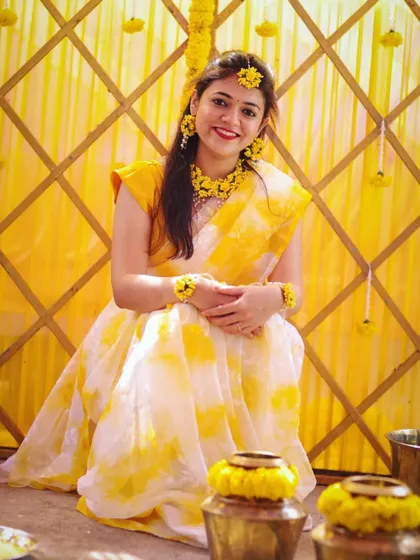 The bride looking radiant in a yellow and white saree, complemented by floral jewelry for her Haldi.