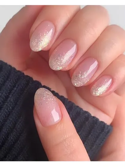 Simple yet stunning. These short, oval nails feature a sheer pink base with a delicate fade of gold glitter from the tip, creating a subtle and elegant sparkle.