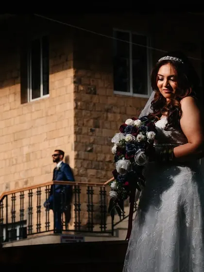 Using natural light and shadow to create a compelling composition. The bride is softly lit in the foreground while the groom stands in the background, creating a sense of story and anticipation.