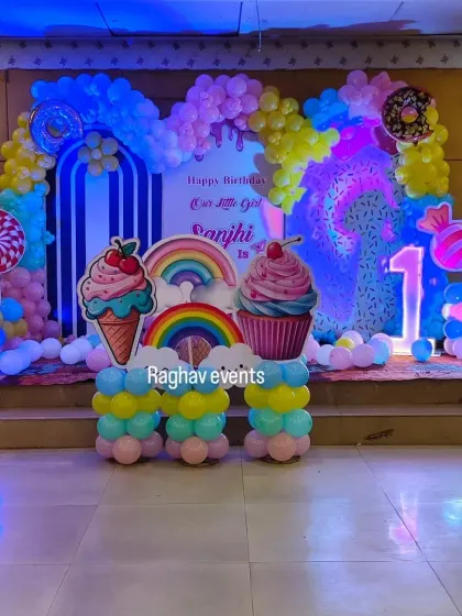A sweet candyland themed first birthday decoration for Sanjhi. The setup includes a large backdrop with ice cream and donut cutouts, a colorful balloon arch, and a light-up number '1'.
