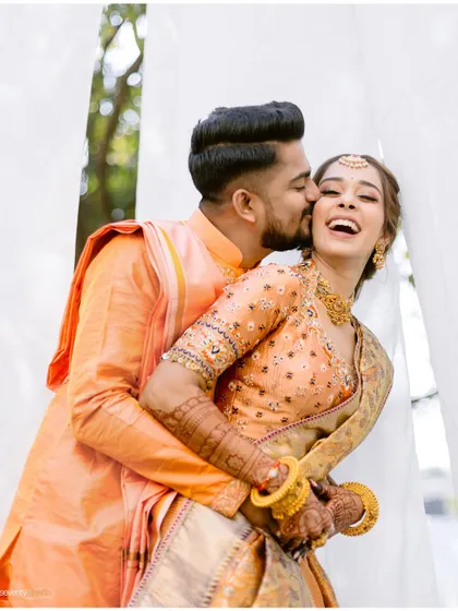 A sweet kiss on the cheek, a moment of pure joy and affection captured during a vibrant Haldi ceremony.