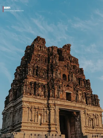 A detailed view of a ruined temple gopuram against a clear blue sky. The image highlights the incredible craftsmanship of the Vijayanagara empire, even in its decaying state.