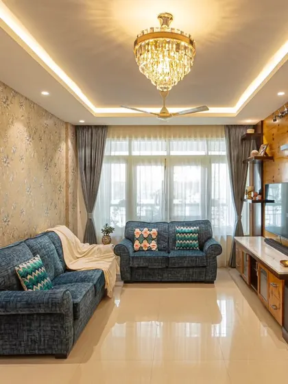 The living room in 'Blue Elegance' after renovation, with reupholstered denim blue sofas and a statement crystal chandelier. The new wallpaper and curtains complete the elegant transformation.