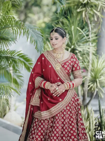 A full-length shot of the bride in her stunning red lehenga, set against a lush green background that makes her colors pop.