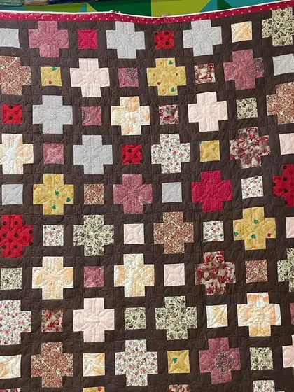 A "Plus" quilt in a charming mix of floral and geometric fabrics against a brown background.