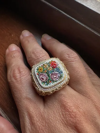 A statement ring showcasing a bouquet of roses in micromosaic art. The detailed floral design is surrounded by a frame of natural diamonds, with a textured gold band that adds to its vintage charm.
