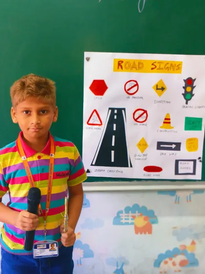 A UKG student teaches his classmates about road safety by explaining various road signs through his well-prepared project.