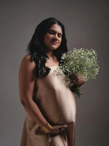 A soft and gentle portrait against a simple grey backdrop. The focus is on the mother's peaceful expression and the delicate baby's breath flowers.