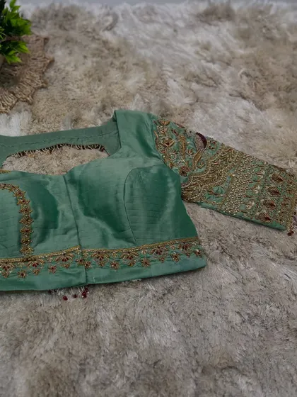 A pastel green blouse with heavy, intricate embroidery featuring peacock motifs in red and gold thread.