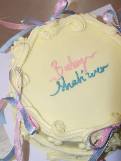 A top-down view of the vintage baby shower cake, highlighting the "Baby Shower" script and the pretty arrangement of pink and blue ribbons.