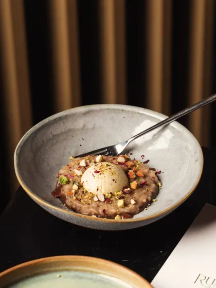 A modern Indian dessert with ice cream, elegantly served in a ceramic bowl. The dark, moody lighting is typical of a fine-dining experience, focusing all attention on the dish.
