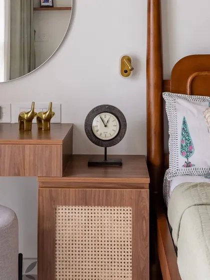 A close-up of the bedside table, which features a wicker-front cabinet and is styled with a modern clock and brass elephants.