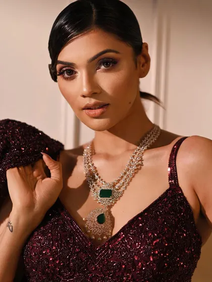 A close-up that focuses on the stunning diamond and emerald necklace, perfectly complementing the deep wine color of the lehenga.