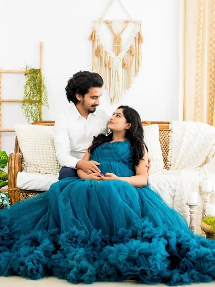 A classic couple's pose on the studio couch, surrounded by lush greenery. The flowing gown and the loving gaze create a romantic and timeless image.