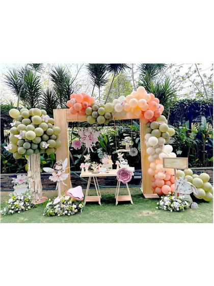 An outdoor enchanted forest setup. This party features a large wooden arch adorned with pastel balloons, balloon trees, and a dessert table filled with whimsical fairy and frog characters.