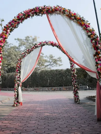 We create stunning floral entrances that make a lasting impression. These twin arches are completely covered in a vibrant mix of pink, orange, and white flowers, with soft drapes adding a touch of elegance to the walkway.
