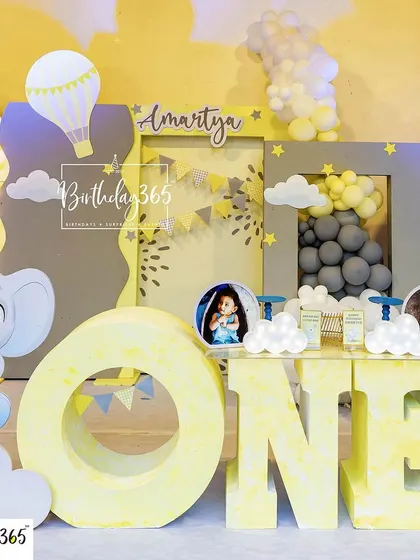 A close-up of a charming hot air balloon and elephant themed first birthday. This shot highlights the large 'ONE' letters for photo opportunities and the custom-designed backdrop with cute illustrations and balloon clouds.