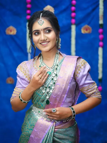 A smiling bride-to-be in a beautiful lavender and green silk saree. The emerald jewelry perfectly complements the outfit, making it ideal for a reception or engagement party.