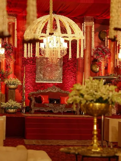 The couple's seating area, framed by cascading floral chandeliers and set against a backdrop of deep red, creating a focal point of regal elegance.