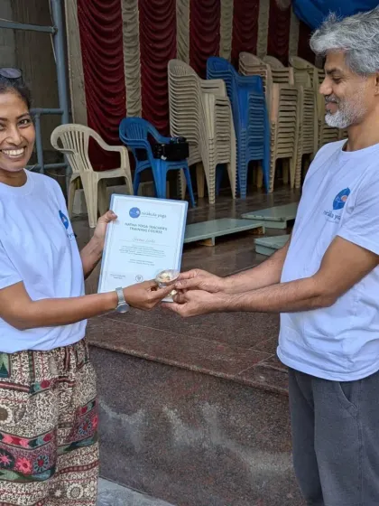A personal moment of achievement. An instructor presents a new teacher with her certificate and a sacred thread, symbolizing the passing of knowledge and the beginning of her journey as a guide for others.