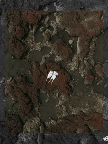 A breathtaking top-down drone photograph of a couple in white, finding a moment of peace on the rustic, rocky shores of Goa.
