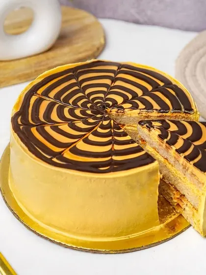 A whole butterscotch cake with a chocolate web design, with one slice ready to be served.