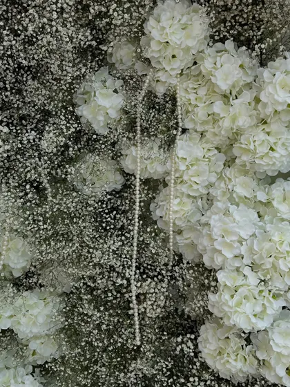 A texture-rich close-up of the floral backdrop, showing the interplay between fluffy baby's breath, white hydrangeas, and delicate pearl strings.